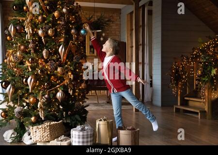 Bonne petite fille mettant une boule de verre sur un arbre de Noël décoré. Banque D'Images