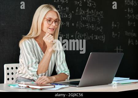Joyeux enseignant ayant en ligne webinar leçon de mathématiques assis au tableau de surveillance. Banque D'Images