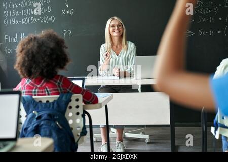 Souriant enseignant heureux ayant cours de maths avec des écoliers assis à un bureau. Banque D'Images