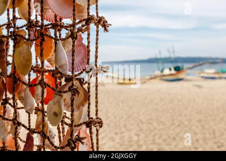 Coquillages colorés sur un filet, souvenirs sur un marché local sur l'île de Boracay, Philippines.Plage de sable, mer et bateaux sur le front de mer. Banque D'Images