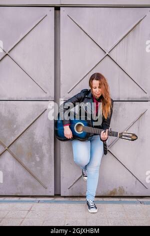 Musicien de rue jouant de la guitare acoustique. Jeune femme portant une veste à l'extérieur Banque D'Images