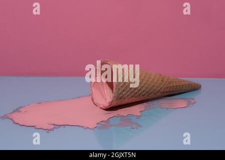 Glace fondue dans un cône. Arrière-plan rose et bleu. Glace acrylique rose. Banque D'Images
