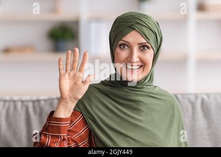 Portrait d'une femme musulmane agitant la main assise à l'intérieur Banque D'Images