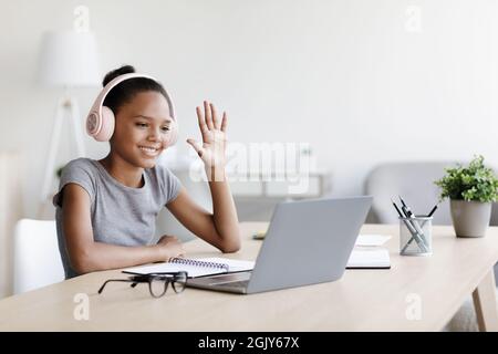 Souriant élève afro-américain dans un casque, regarder une leçon vidéo, passer un appel à distance et passer la main sur un ordinateur portable Banque D'Images