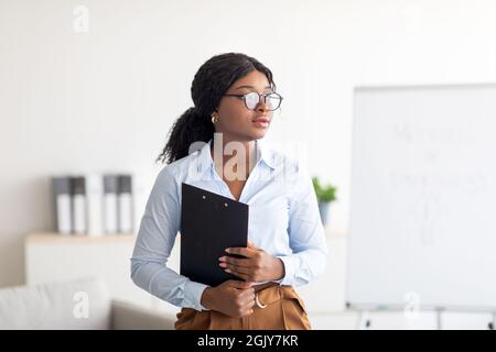 Portrait d'une psychothérapeute féminine noire concentrée avec presse-papiers regardant de côté en profondeur dans la pensée au bureau moderne Banque D'Images