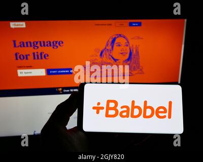 Personne tenant un smartphone avec le logo de la société d'apprentissage de la langue allemande Babbel GmbH sur l'écran devant le site Web. Mise au point sur l'affichage du téléphone. Banque D'Images