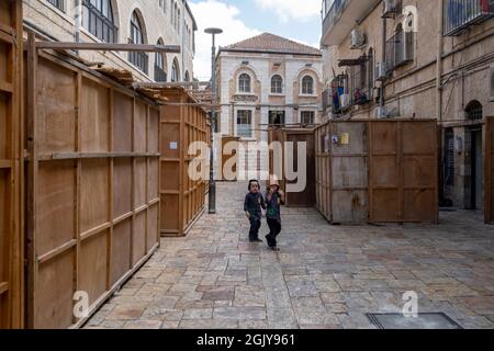 Les enfants juifs orthodoxes marchent dans une rue pleine de huttes traditionnelles temporaires en bois de 'Sukkot' construites pour être utilisées pendant la semaine du festival juif de Sukkot ou de Sukkoth dans le quartier juif de Batei Ungarin Haredi près de l'enclave ultra-orthodoxe de MEA Shearim dans l'ouest de Jérusalem Israël Banque D'Images
