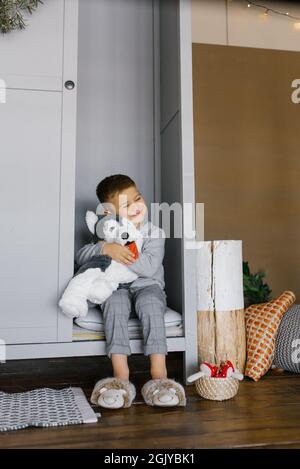 Un petit garçon est assis dans le placard et embrassant son jouet doux préféré, il est heureux et souriant Banque D'Images