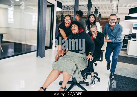 Les hommes d'affaires sans souci s'amusent dans un lieu de travail moderne. Groupe de collègues joyeux se poussant les uns les autres sur des chaises dans un bureau créatif.Happy business Banque D'Images