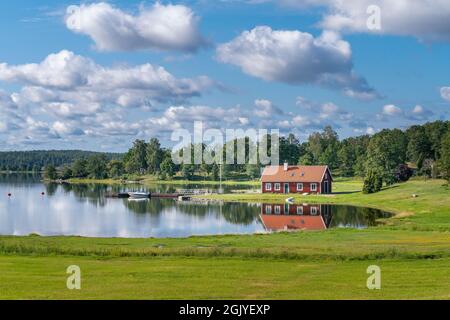 Maison typique en bois rouge dans la campagne au bord de la mer dans le natre du sud de la Suède, lors d'une belle journée ensoleillée d'été. Paysage rural relaxant. Réflexion Banque D'Images