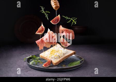 Crostini au prosciutto ricotta et figues, jambon italien volant et fruits sur fond sombre, toast avec jamon, gros plan. Banque D'Images