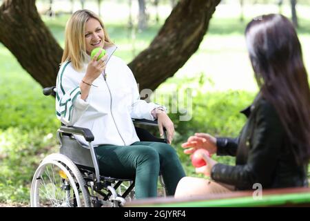 Femme handicapée en fauteuil roulant mangeant de la pomme avec son ami dans le parc Banque D'Images