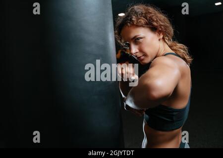 Femme dans une posture de combat sur fond noir avec un sac de boxe. Banque D'Images