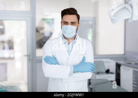 Médecin de sexe masculin dans un masque facial debout à la clinique dentaire Banque D'Images