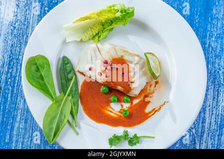 Filet de morue à la vapeur avec sauce paprika et feuilles de salade. Banque D'Images