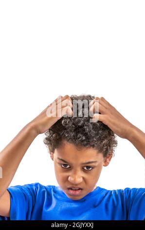 Jeune garçon souriant se grattant les cheveux pour les poux ou les allergies. Banque D'Images