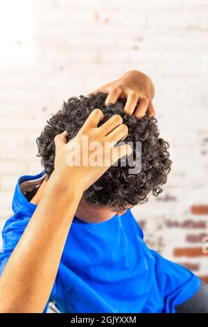 Jeune garçon souriant se grattant les cheveux pour les poux ou les allergies. Banque D'Images