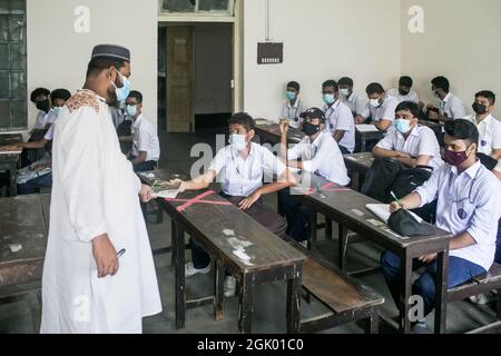 Les élèves portant des masques de protection contre la propagation du coronavirus sont assis dans une salle de classe à l'école préparatoire et au collège de Mohammadpur. Après près de 18 mois, les candidats au certificat d'enseignement primaire (PEC), au certificat d'enseignement secondaire (SSC) et au certificat d'enseignement secondaire supérieur (HSC) ont commencé à assister aux cours dimanche, alors que les écoles et les collèges ont rouvert avec une foule de protocoles de sécurité Covid en place. La décision de reprendre les cours et les examens en personne a été prise par le gouvernement au début du mois en vue de l'amélioration de la situation de Covid-19 autour du Bangladesh. Tous les insti éducatifs Banque D'Images