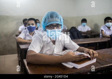 Les élèves portant des masques de protection contre la propagation du coronavirus sont assis dans une salle de classe à l'école préparatoire et au collège de Mohammadpur. Après près de 18 mois, les candidats au certificat d'enseignement primaire (PEC), au certificat d'enseignement secondaire (SSC) et au certificat d'enseignement secondaire supérieur (HSC) ont commencé à assister aux cours dimanche, alors que les écoles et les collèges ont rouvert avec une foule de protocoles de sécurité Covid en place. La décision de reprendre les cours et les examens en personne a été prise par le gouvernement au début du mois en vue de l'amélioration de la situation de Covid-19 autour du Bangladesh. Tous les insti éducatifs Banque D'Images