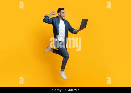 Homme arabe émotionnel utilisant un nouveau PC portable moderne sur jaune Banque D'Images