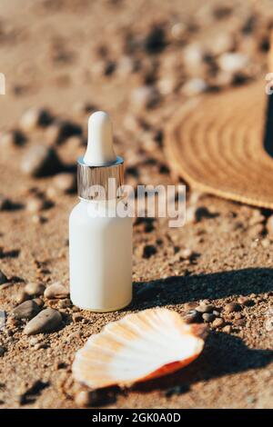 Hydratant cosmétique, bouteille d'huile ou de sérum dans le sable de plage à côté de la mer et chapeau de paille. Cosmétiques naturels, concept de cosmétiques de crème solaire. Gros plan. Banque D'Images