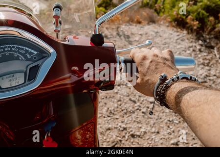 Les mains de l'homme sur le volant, le mec conduisant un mobylette ou un scooter, vue rapprochée. Le conducteur conduit une moto rouge rétro. Guidon de moto. Banque D'Images