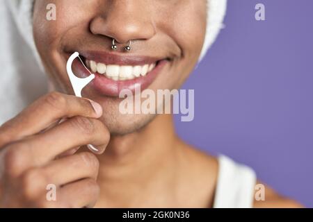 Homme transgenre en gros plan avec fil dentaire souriant sur fond violet. Afroamerican trans genre Banque D'Images