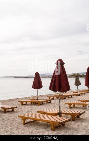 Transats en bois vides et parasols pliés sur le sable près de la mer Égée. Lounge Chill zone sur la plage de la ville à Athènes, Grèce Banque D'Images