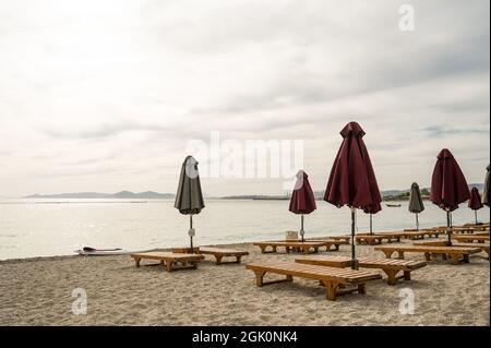 Transats en bois vides et parasols pliés sur le sable près de la mer Égée. Lounge Chill zone sur la plage de la ville à Athènes, Grèce Banque D'Images