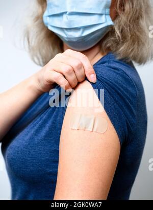 Jeune femme vaccinée montrant le bras avec du plâtre, femme sous masque après avoir reçu le vaccin COVID-19. Concept de personnes corona virus vaccination, inj Banque D'Images