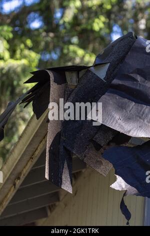 Les bardeaux desserrés sont mis au rebut sur le toit qui est pendé sur le bord Banque D'Images