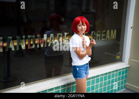 L'actrice adolescente de Cosplay asiatique devant la boutique de crèmes glacées | l'actrice de Cosplay de globules rouges devant la boutique Banque D'Images