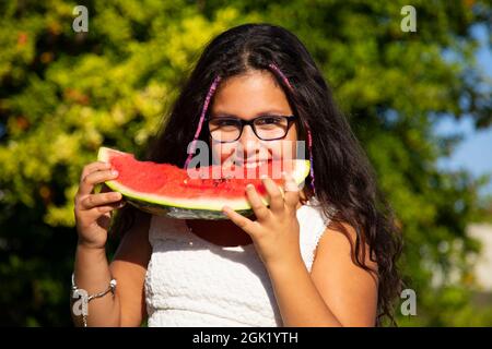 une fille gitane aux cheveux longs noirs mange la grande tranche de pastèque Banque D'Images