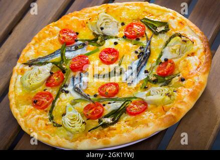 Pizza savoureuse avec anchois, fromage, tomates séchées, artichauts à table Banque D'Images