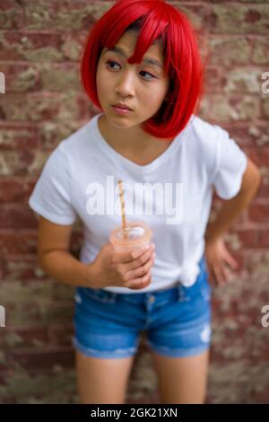 L'actrice adolescente Cosplay debout devant le mur de briques | Asian Girl with Red Wig Banque D'Images