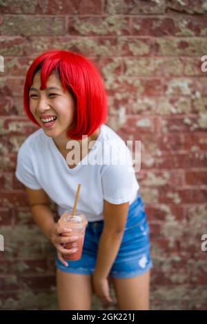 L'actrice adolescente Cosplay debout devant le mur de briques | Asian Girl with Red Wig Banque D'Images