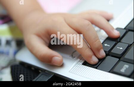 La main d'enfant tient une souris ou un clavier d'ordinateur. L'enfant apprend en ligne et joue sur l'ordinateur à la maison. École, éducation, technologie. Banque D'Images