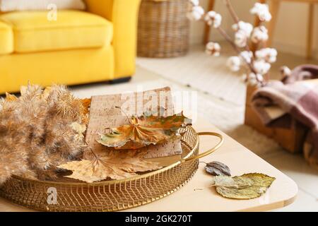 Plateau avec feuilles d'automne, branches en roseau et livre sur table à l'intérieur de la salle de séjour, gros plan Banque D'Images