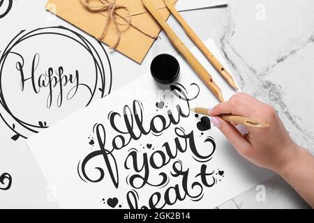 Femme écrivant du texte SUIVEZ VOTRE COEUR sur fond clair Banque D'Images