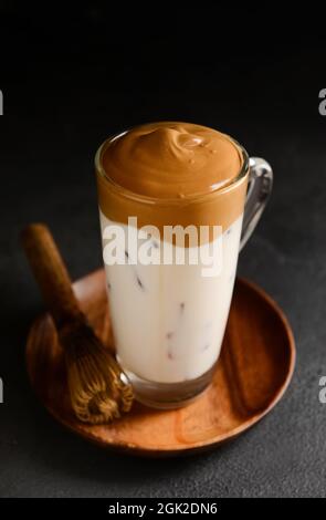 Tasse en verre de savoureuse Dalgona hojicha latte et chasen sur fond sombre Banque D'Images