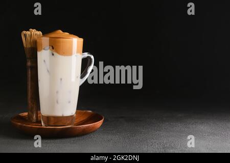 Tasse en verre de savoureuse Dalgona hojicha latte et chasen sur fond sombre Banque D'Images