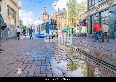 Amsterdam pays-Bas - août 20 2017; tram électrique de transport public entrant dans la rue de la ville avec des personnes marchant et à vélo . Banque D'Images