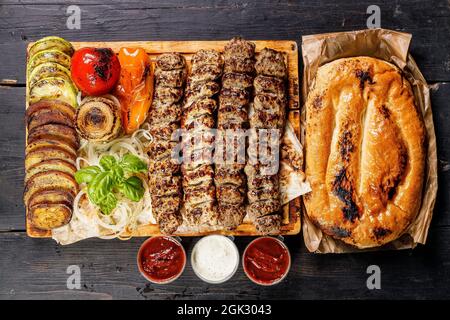 Assortiment de kebabs de différents types de viande. Veau, poulet, kebabs d'agneau avec légumes et sauces sur une planche de bois. Cuisine traditionnelle turque de rue Banque D'Images