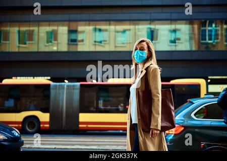 Femme portant un masque de protection dans la ville. Une femme en manteau marche dans la rue de la ville pendant le confinement pandémique Covid-19 Banque D'Images