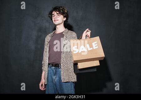 Portrait d'un jeune homme élégant avec des sacs en papier regardant l'appareil photo debout sur fond noir Banque D'Images
