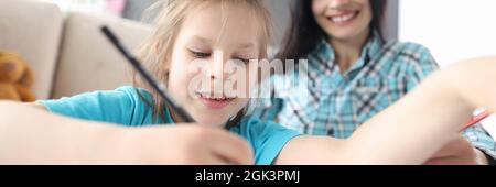 Petite fille tire avec des crayons sur fond assis femme Banque D'Images