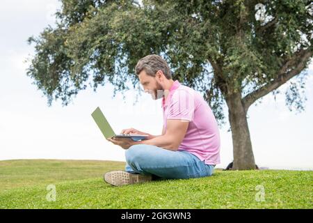 freelance man post blog en ligne s'assoir sur l'herbe. écriture en ligne. homme d'affaires utilisant un ordinateur portable pour bloguer. Banque D'Images