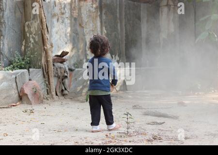 Gros plan vue arrière photo d'Un petit enfant indien jouant de la boue et de la poussière en hiver et portant un chandail bleu Banque D'Images