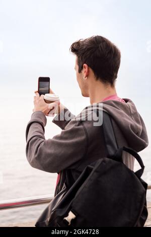 vue arrière d'un jeune étudiant avec sac à dos et café prendre une photo avec un téléphone mobile, concept de technologie et style de vie millénaire, espace de copie f Banque D'Images