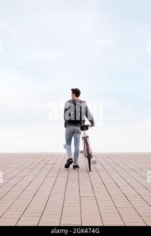 vue arrière d'un jeune homme marchant tout en poussant un vélo, concept de transport écologique et durable, espace de copie pour le texte, photo verticale Banque D'Images
